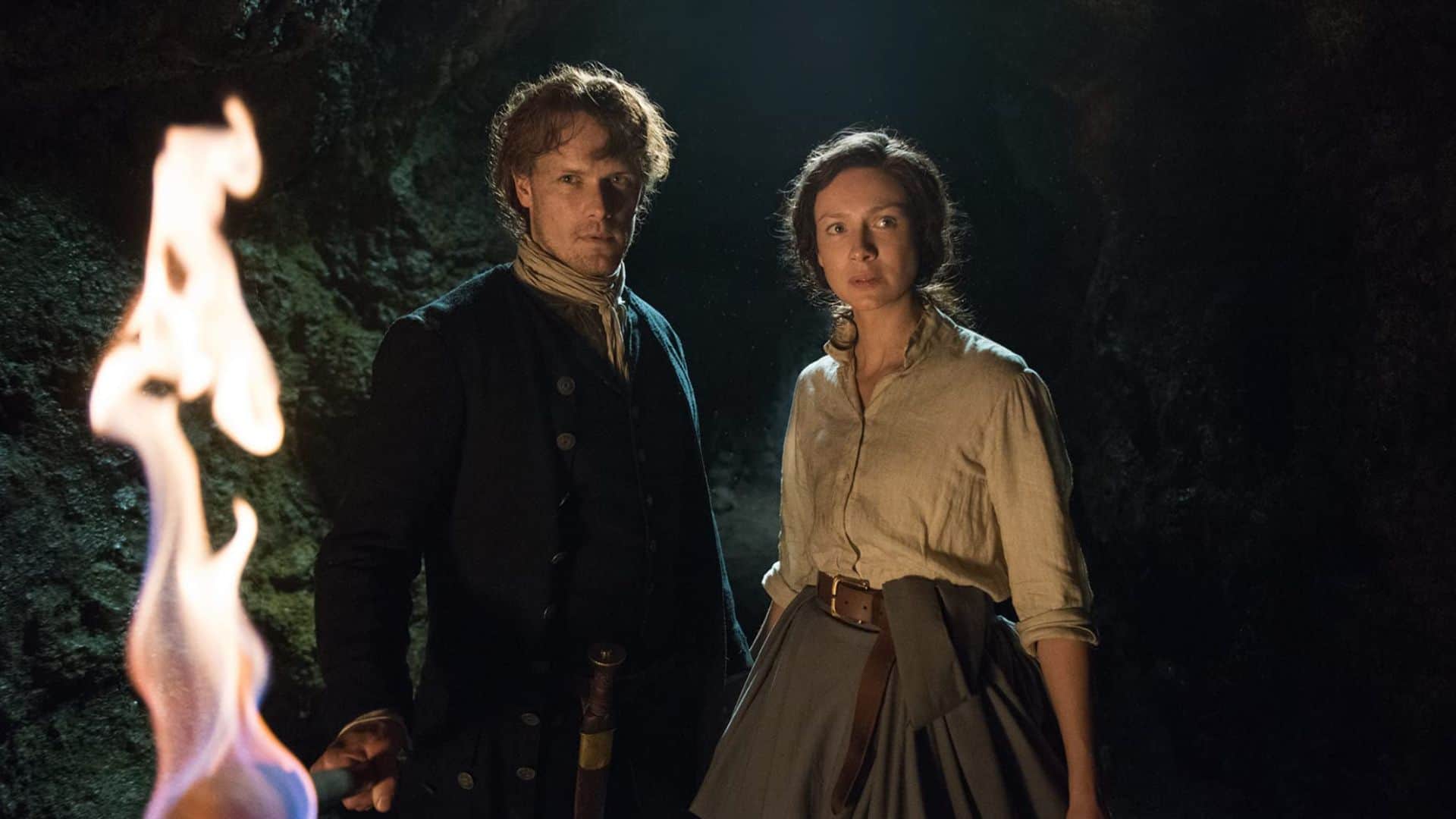 Jaime and Claire in 18th-century clothing next to a fire in this image from Netflix