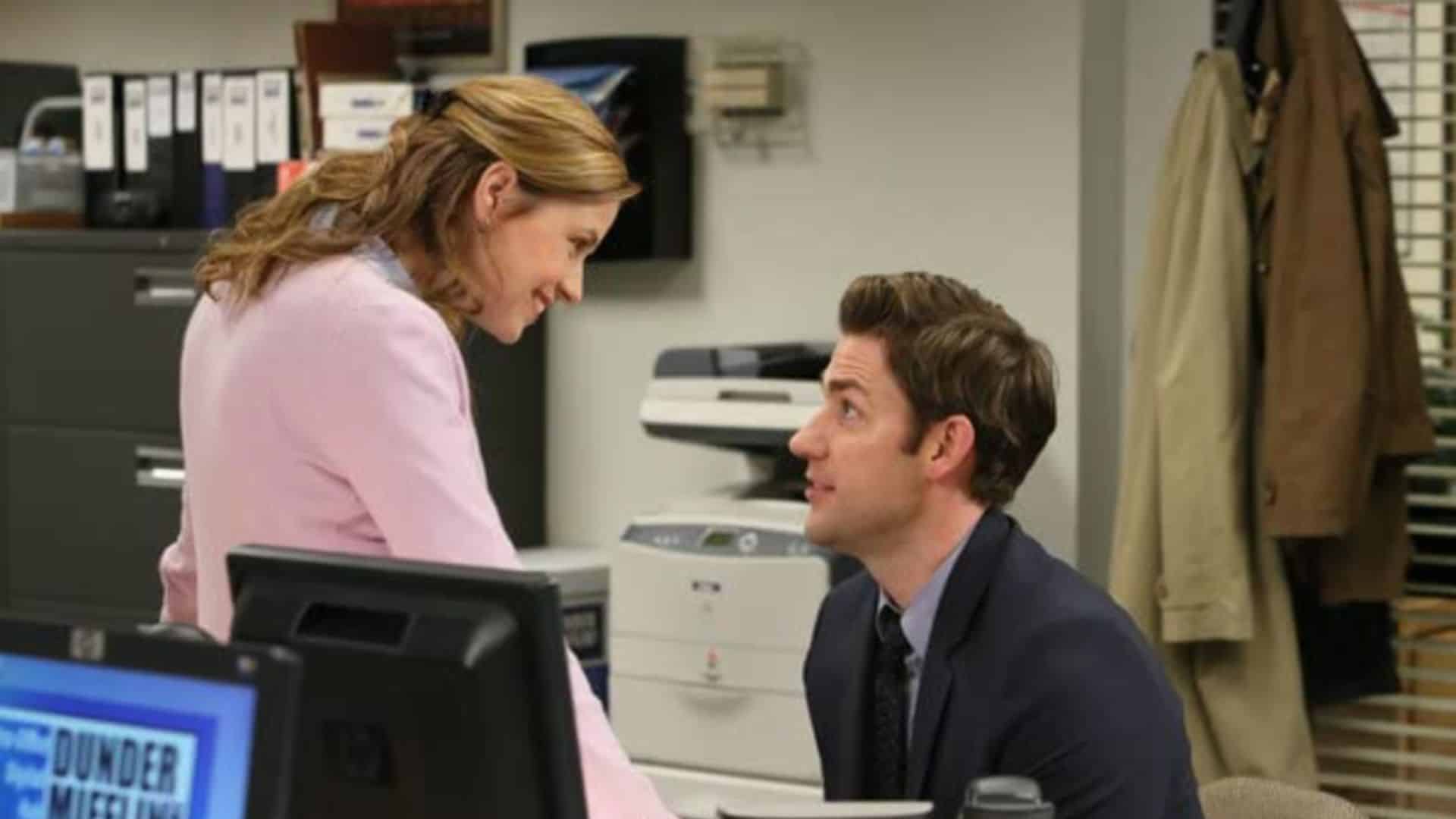Pam and Jim talk at a desk in the office in this image from Peacock